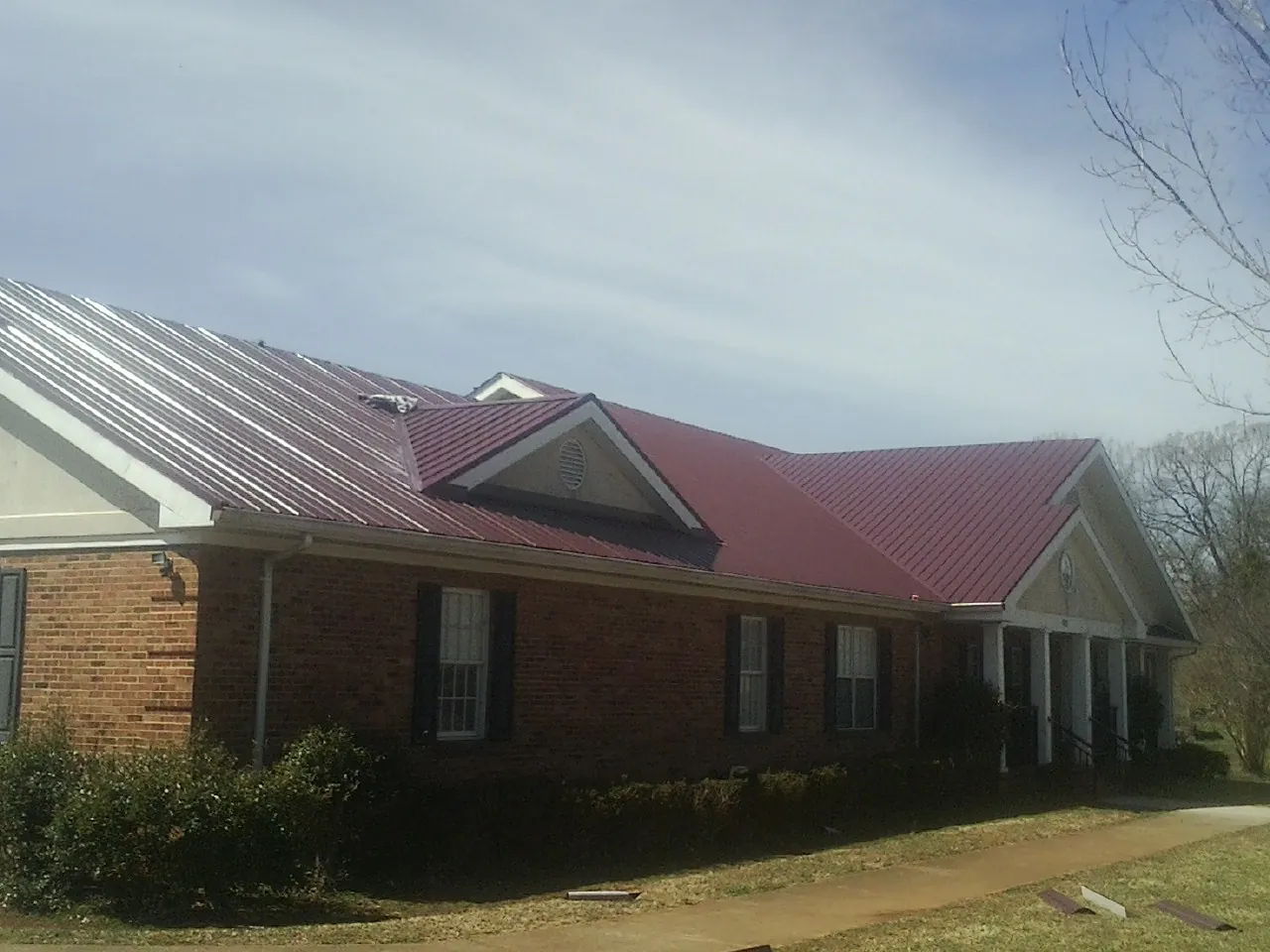 Red metal roof with gabled entries on a long brick building, from a Hail Damage Roof Repair job in Lewisport