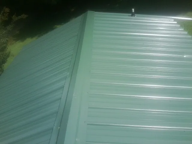 New green metal panels meeting at the ridge of a roof — Flat Roof Repair work by our crew in Lewisport