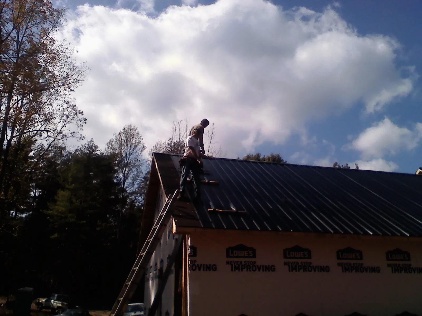Roofer fastening dark metal panels high against a cloudy sky, from a Roof Inspection job in Lewisport