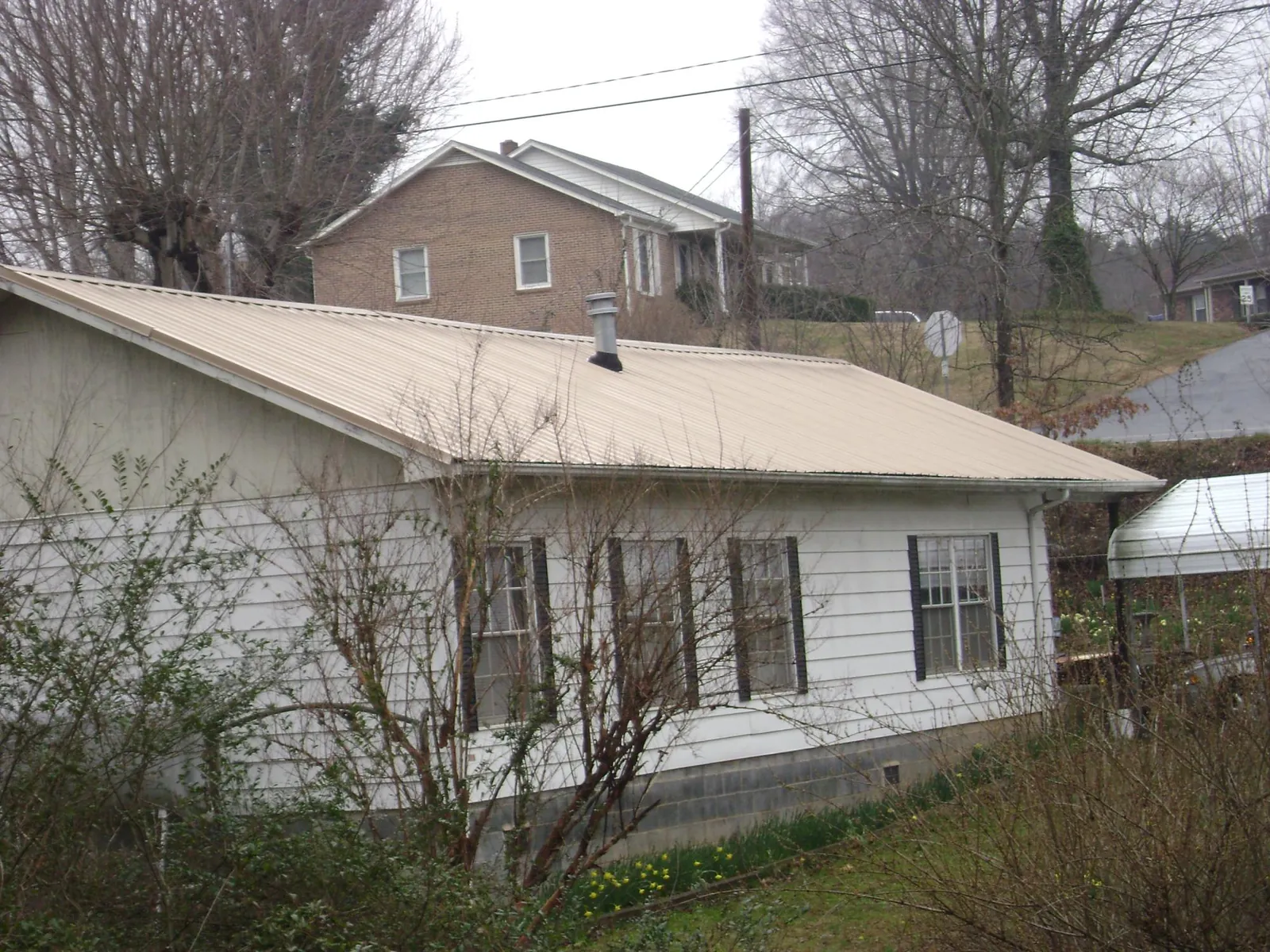 Tan metal roof on a white sided house set into a hillside — Commercial Roofing by Roofing Brothers in Lewisport